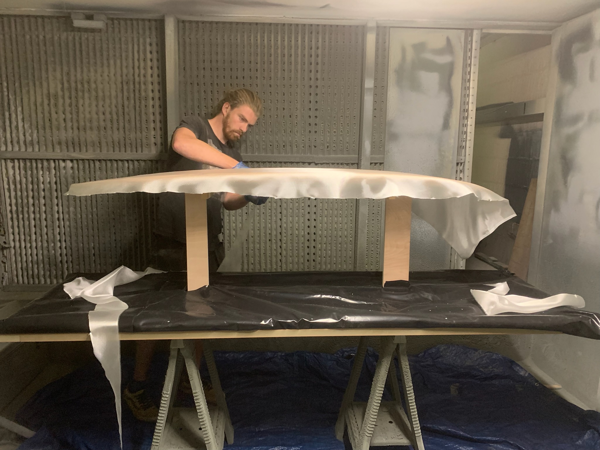 Board maker laying fibreglass cloth over a surfboard in a finishing room