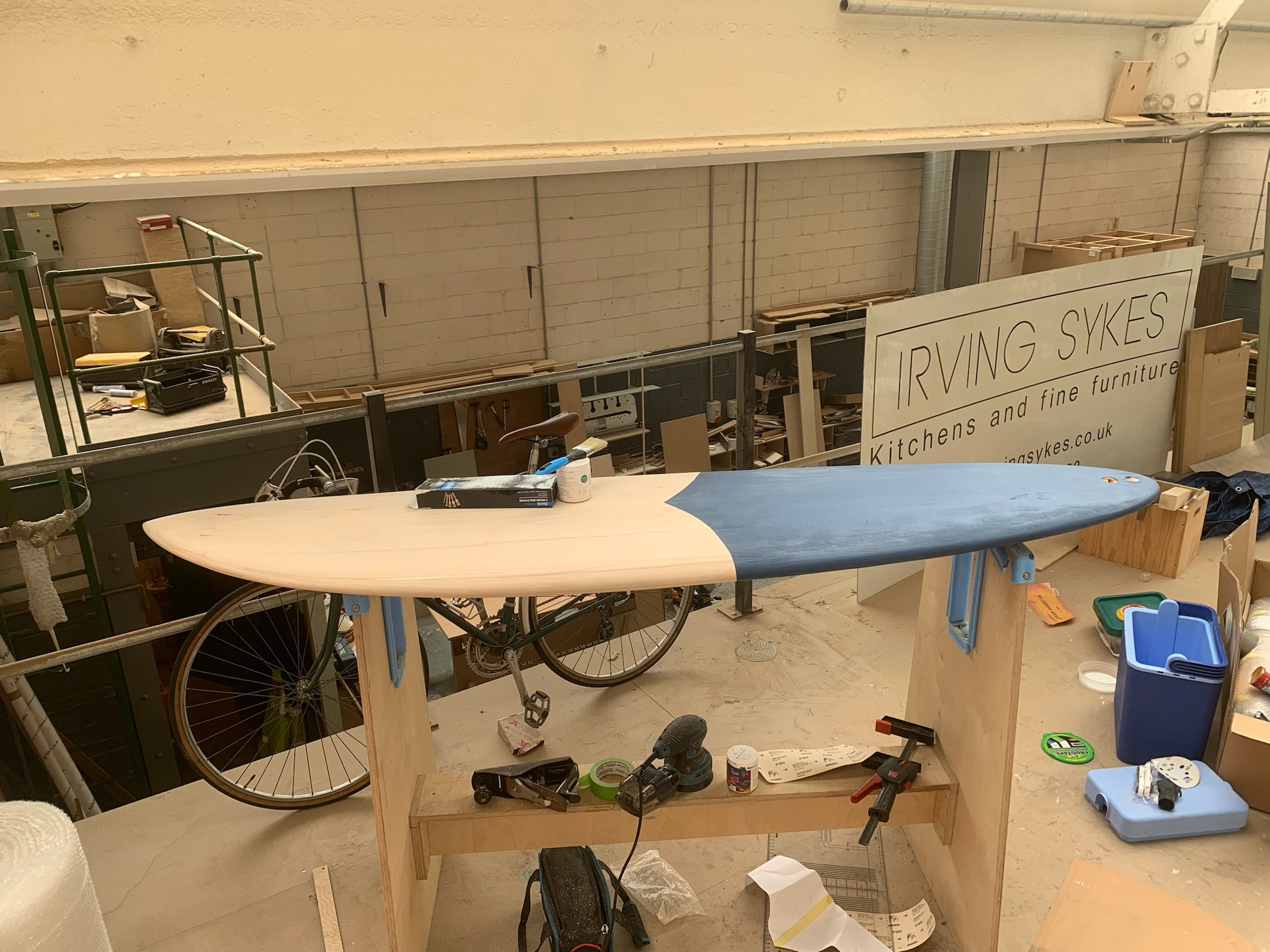 Timber surfboard in the workshop with the first section of blue colour applied